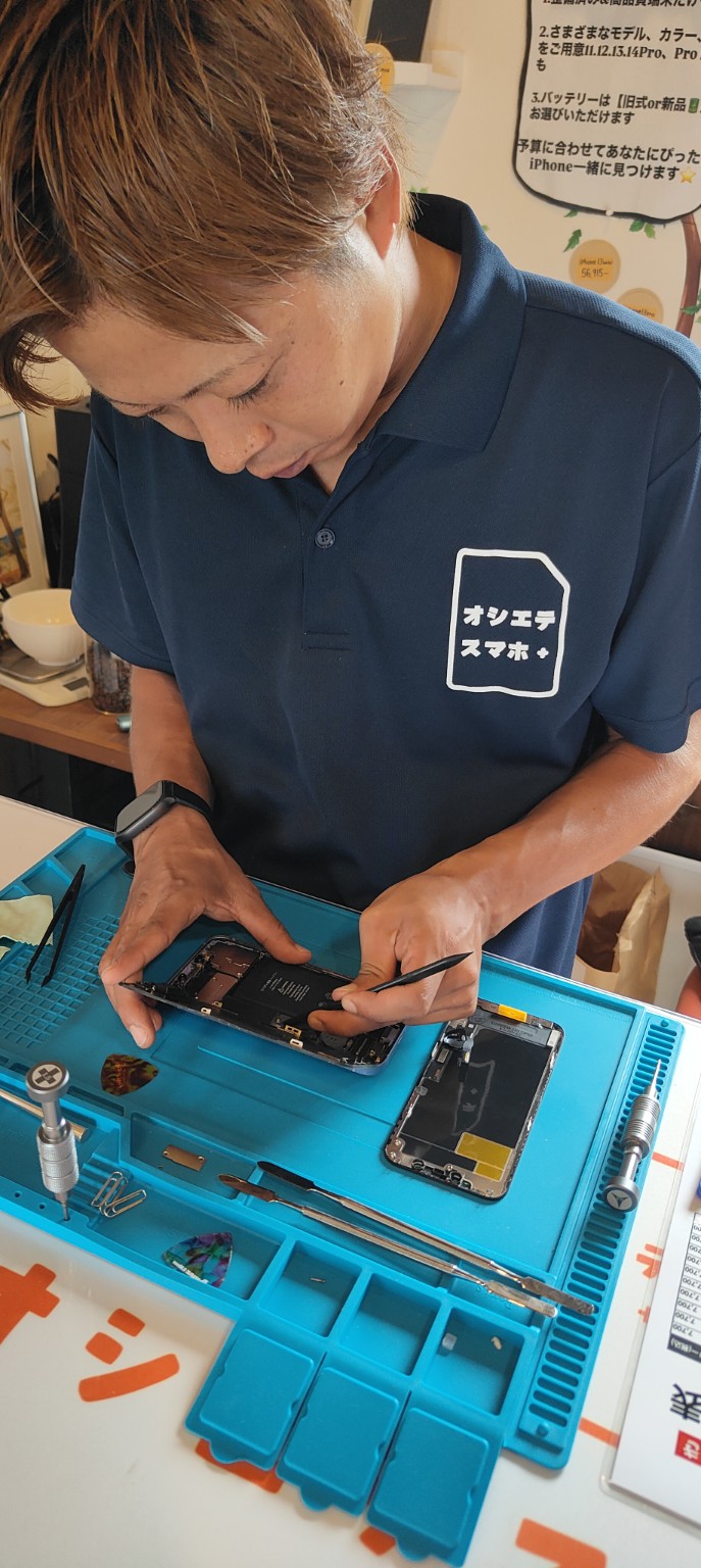 青い作業マットの上でiPhoneを真剣に修理するネイビーのシャツの男性スタッフ