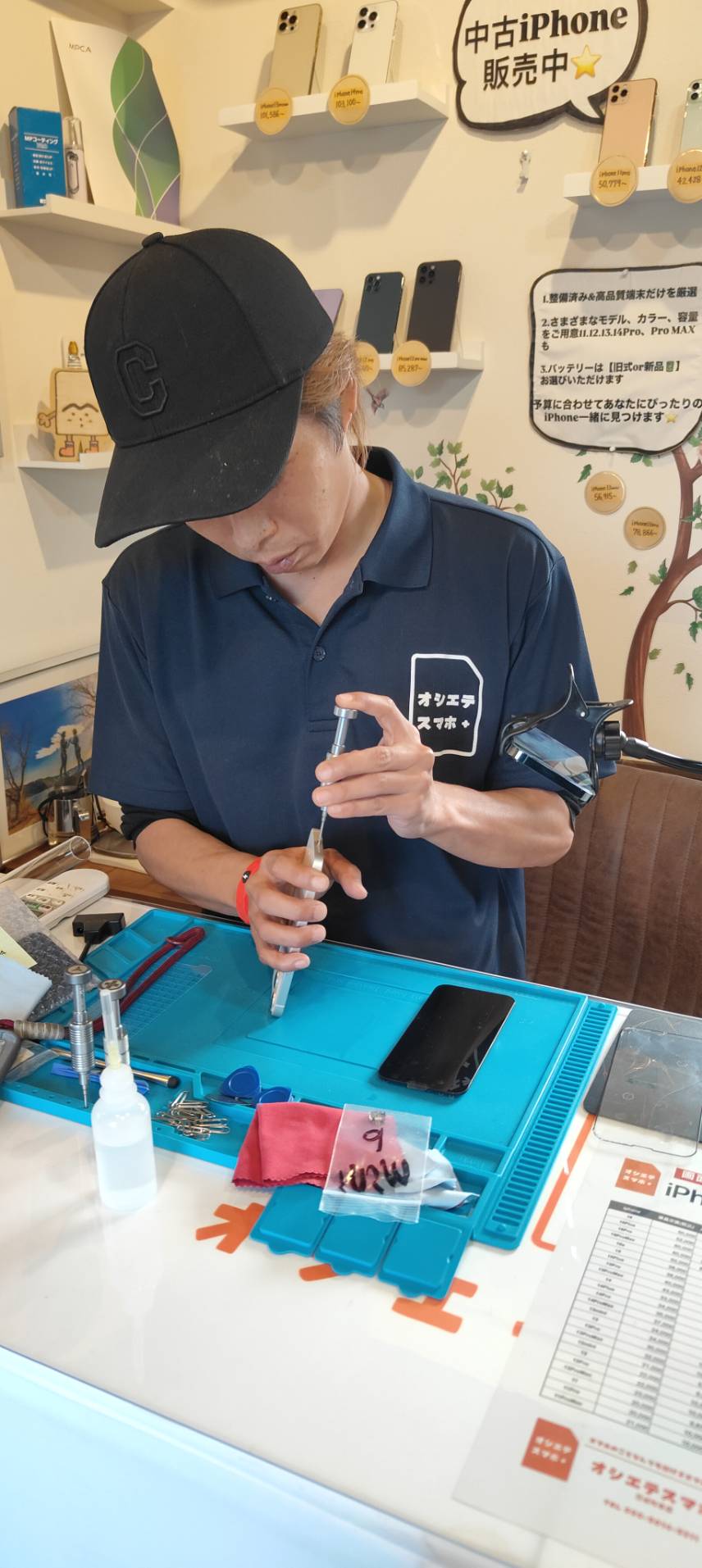 ネイビーの服を着たスタッフが立った状態でスマホを修理する様子